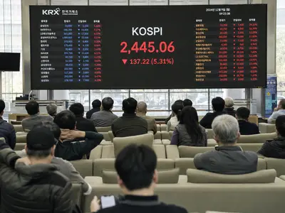 A wide interior shot of retail investors seated in a Seoul securities brokerage watching a large electronic board displaying tumbling KOSPI figures in red, natu