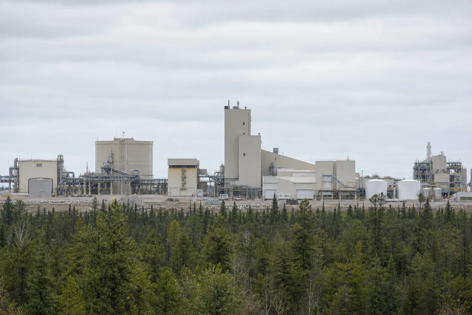A wide daylight view of the McClean Lake uranium mill complex in northern Saskatchewan, its metal processing buildings, storage tanks and pipework standing amid
