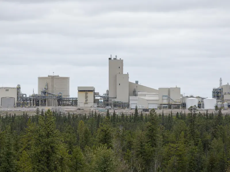 A wide daylight view of the McClean Lake uranium mill complex in northern Saskatchewan, its metal processing buildings, storage tanks and pipework standing amid
