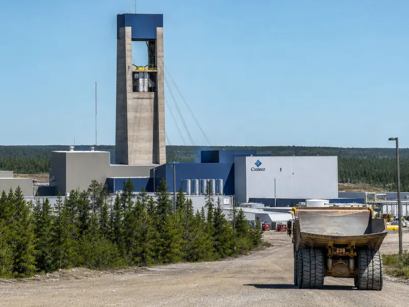A wide daylight establishing shot of the Cigar Lake uranium mine's surface headframe and processing buildings in the northern Saskatchewan forest, with Cameco b