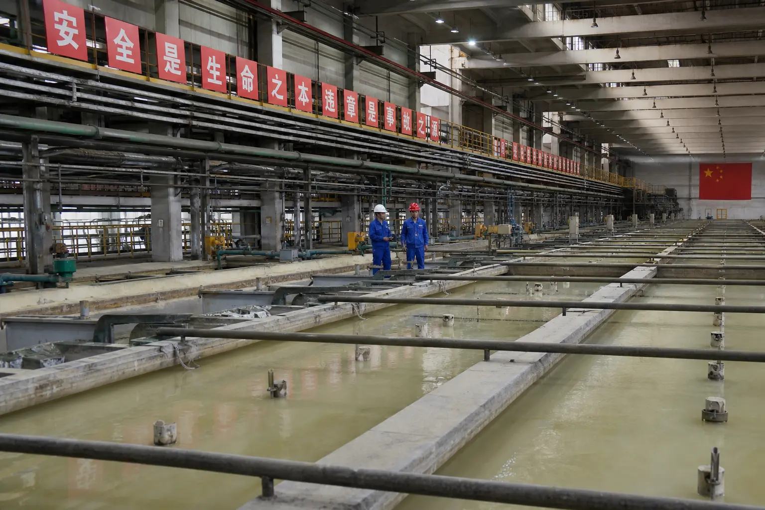 Interior of a rare earth separation plant in Baotou, Inner Mongolia, long rows of mixer-settler tanks receding down the hall, pale chemical liquor in the open c