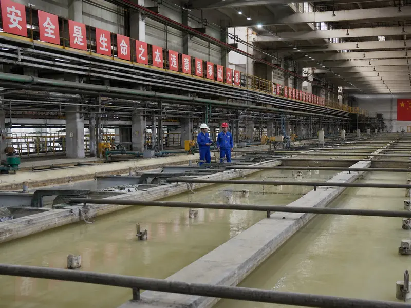 Interior of a rare earth separation plant in Baotou, Inner Mongolia, long rows of mixer-settler tanks receding down the hall, pale chemical liquor in the open c