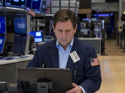 A trading floor at the New York Stock Exchange seen straight-on in ordinary daylight, with traders at their terminals during a working session.