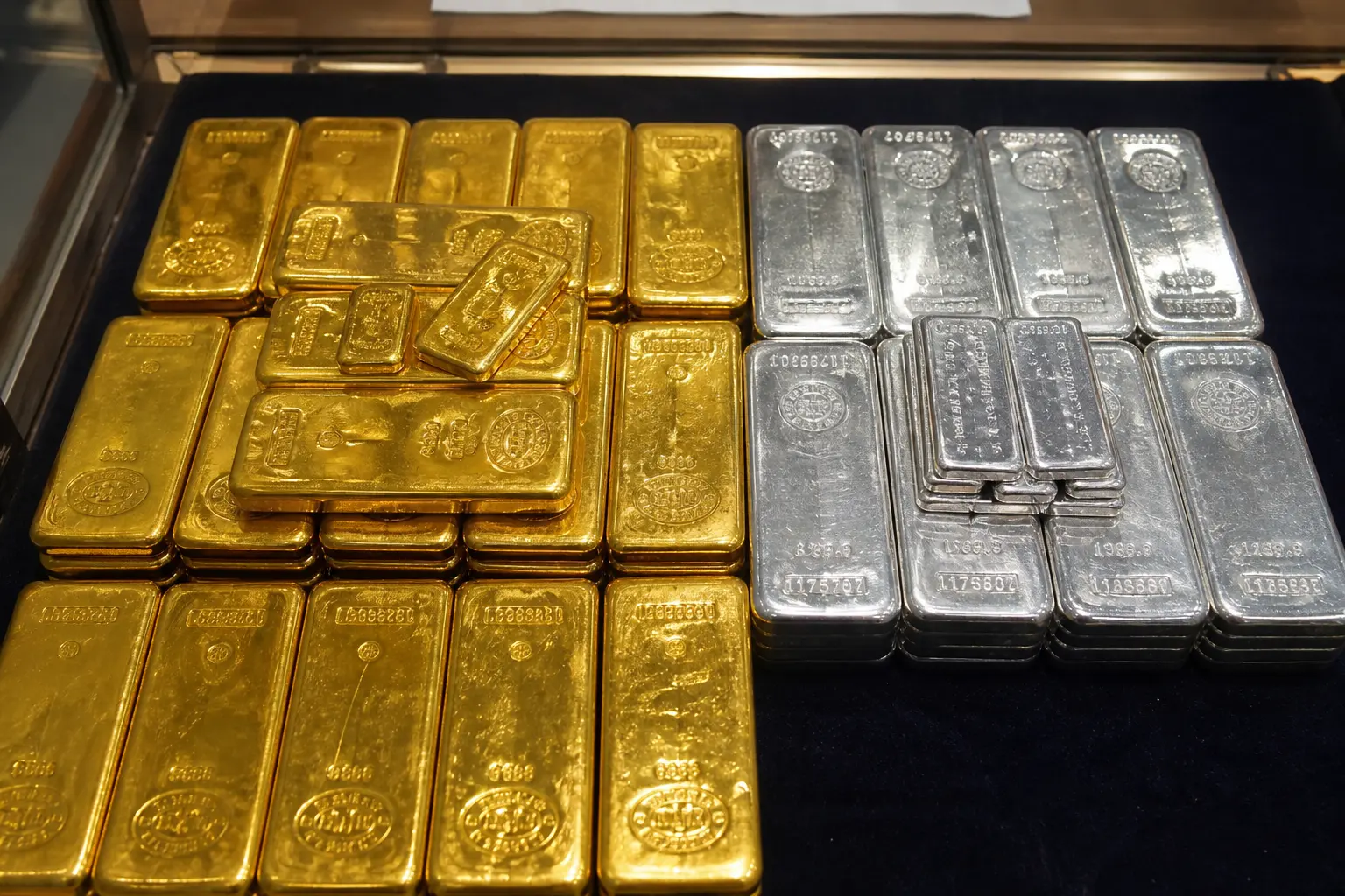 A close, top-down view of stacked gold and silver bars resting on a dealer's counter under plain overhead light.