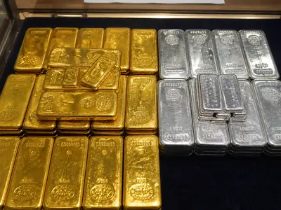 A close, top-down view of stacked gold and silver bars resting on a dealer's counter under plain overhead light.
