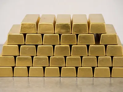 A neatly stacked row of refined gold bullion bars photographed head-on on a plain surface under even daylight.