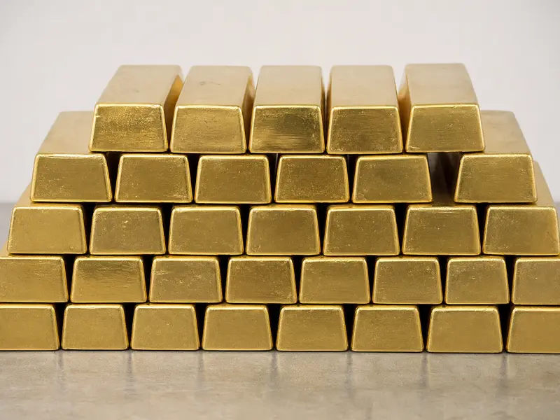 A neatly stacked row of refined gold bullion bars photographed head-on on a plain surface under even daylight.