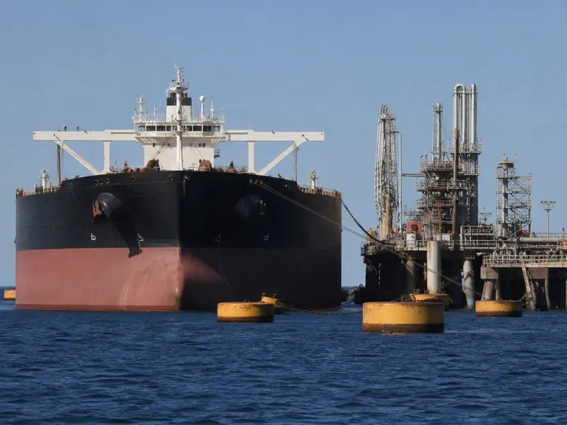 A wide daylight shot of a large crude oil tanker moored at an offshore Gulf loading terminal with pipelines and mooring buoys in calm water, taken from sea leve