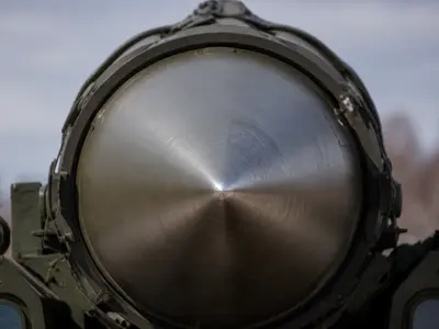 A tight close-up of the polished metal nosecone tip of a ballistic missile mounted on its transporter, the heat-resistant alloy surface catching daylight, with