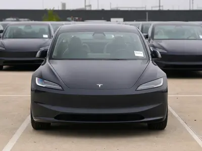 A row of new Tesla vehicles parked head-on in an outdoor delivery lot under flat daylight.