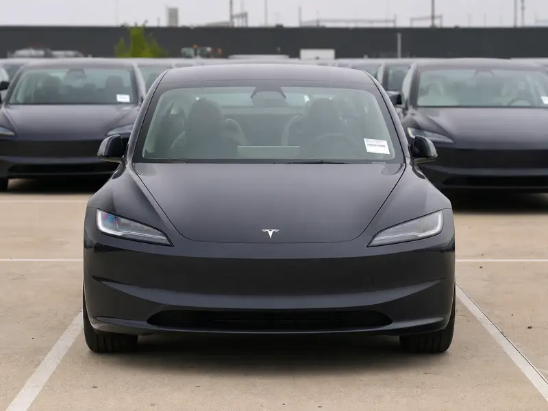 A row of new Tesla vehicles parked head-on in an outdoor delivery lot under flat daylight.