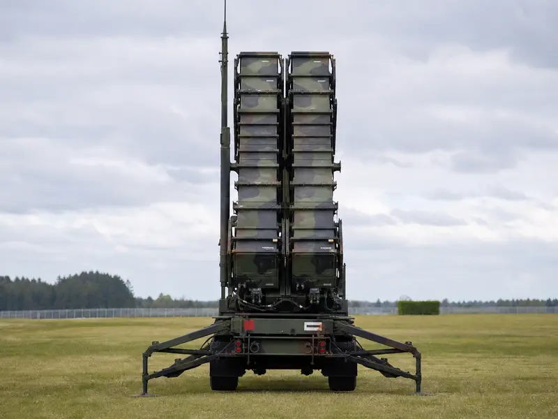 A Patriot missile defense launcher stands in an open field under flat daylight, photographed straight-on with its launch tubes raised toward the sky.