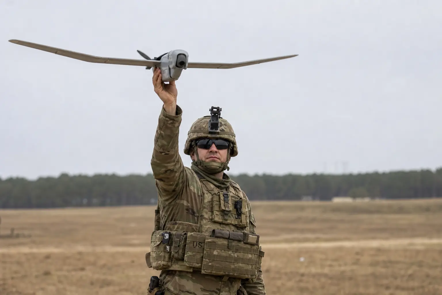 U.S. Army soldiers in fatigues launching a small hand-held reconnaissance drone during a training exercise on an open field under flat daylight.